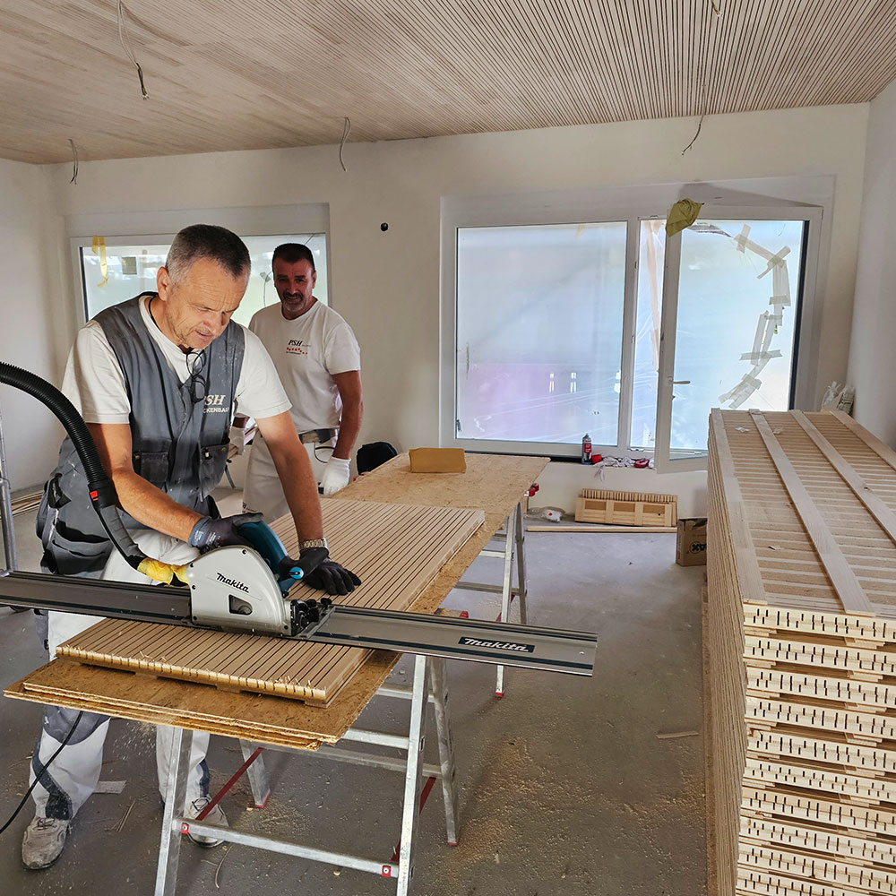 Zwei Handwerker schneiden Akustik- oder Holzpaneele auf einer Baustelle pr&auml;zise zu.